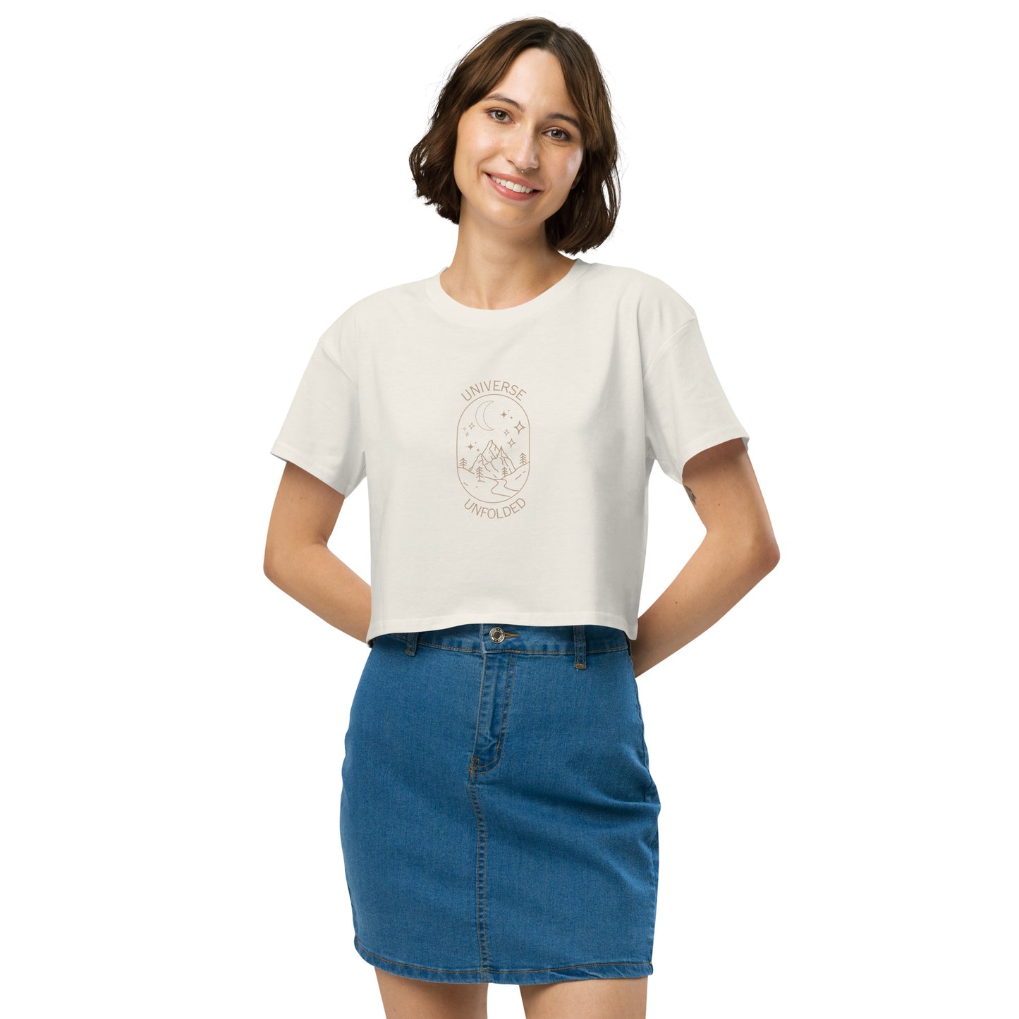 Cheerful woman in a ecru crop top with 'UNIVERSE UNFOLDER' and celestial design, paired with a denim skirt.