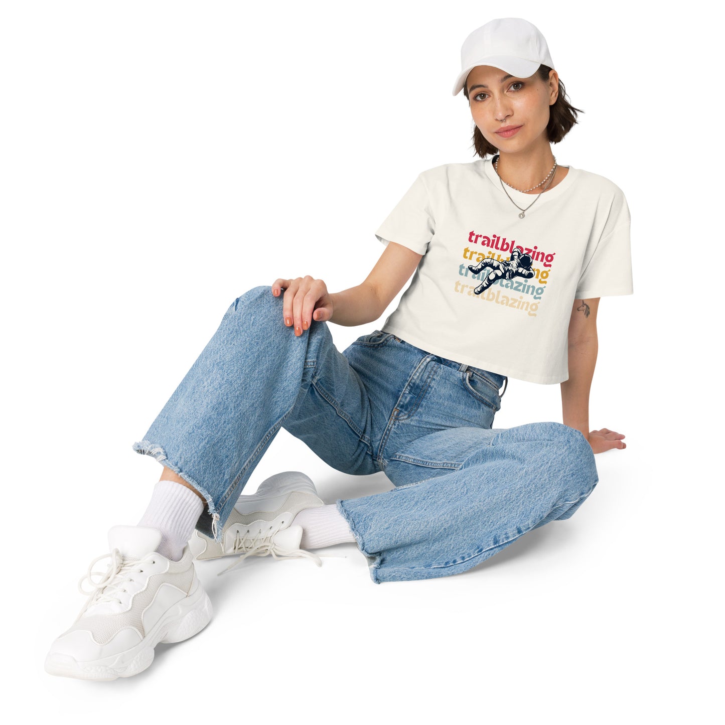 Relaxed woman in a ecru crop top with a trailblazing graphic, paired with baggy denim jeans and white sneakers, ready to make a statement.