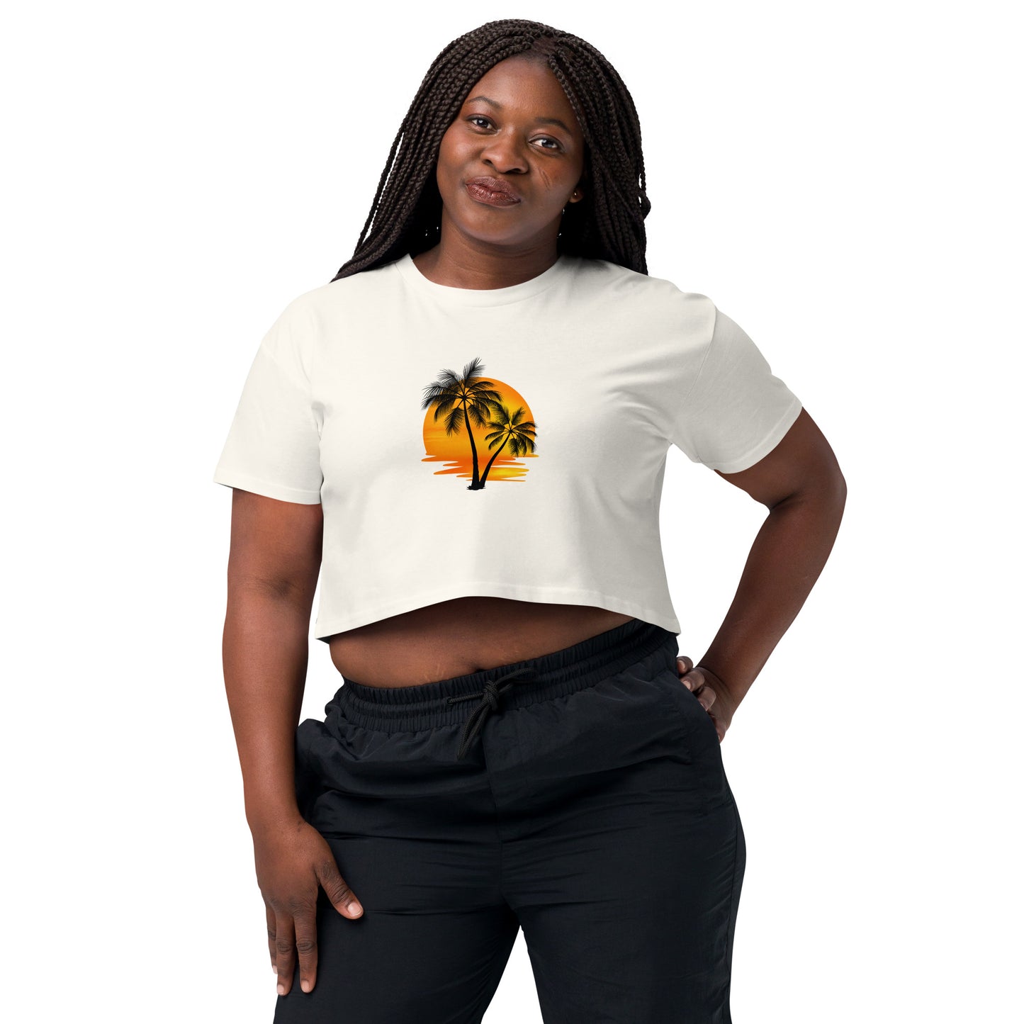 Smiling woman in a ecru crop top featuring a palm tree silhouette against a sunset, paired with casual black trousers for a laid-back, tropical-inspired look.