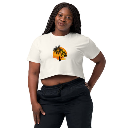 Smiling woman in a ecru crop top featuring a palm tree silhouette against a sunset, paired with casual black trousers for a laid-back, tropical-inspired look.