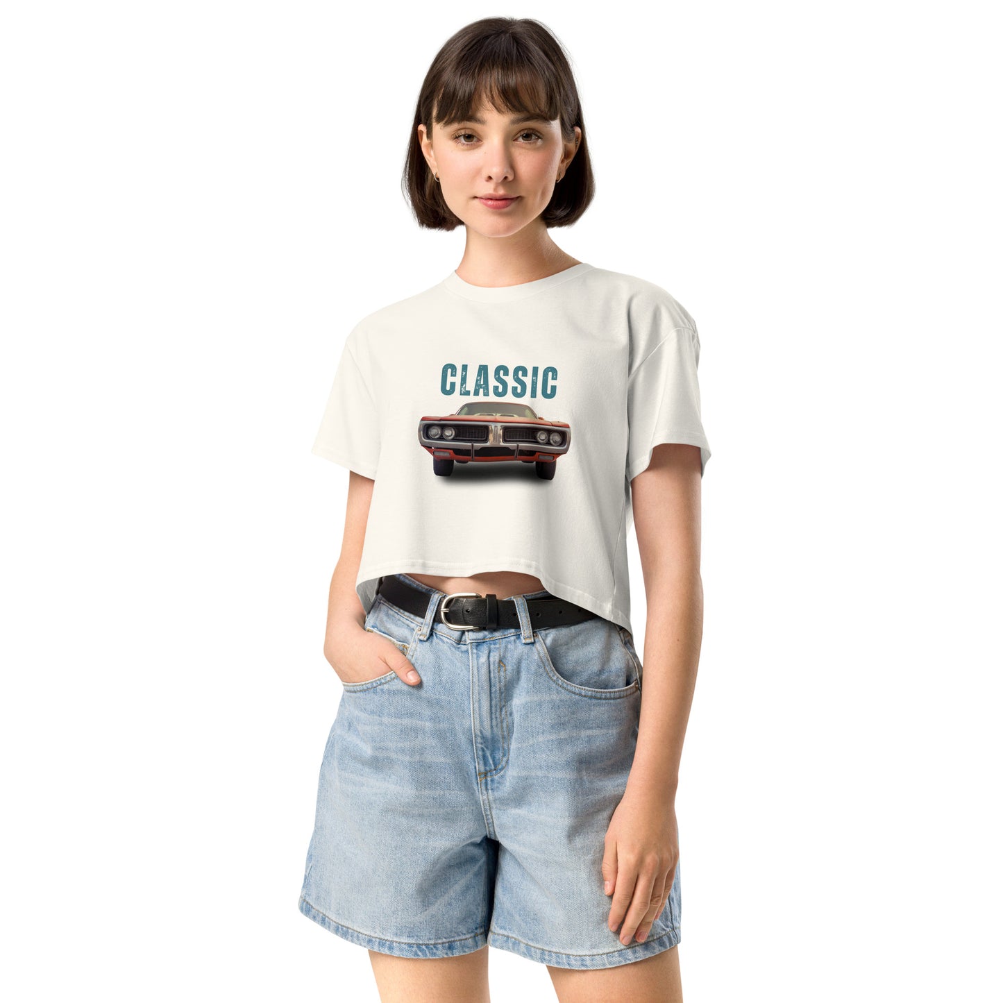 Young woman sporting a ecru crop top with a classic car graphic design and 'CLASSIC' text, paired with blue denim shorts for a relaxed yet fashionable look.