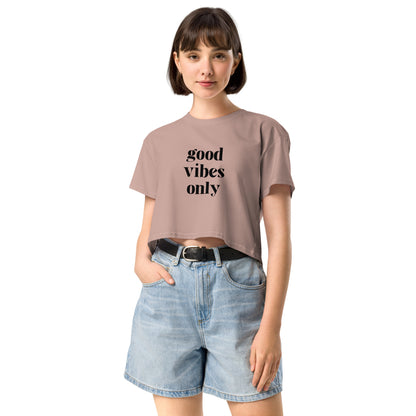 Content woman in a hazy pink crop top with 'good vibes only' text, coupled with light blue denim shorts, conveying a laid-back style.