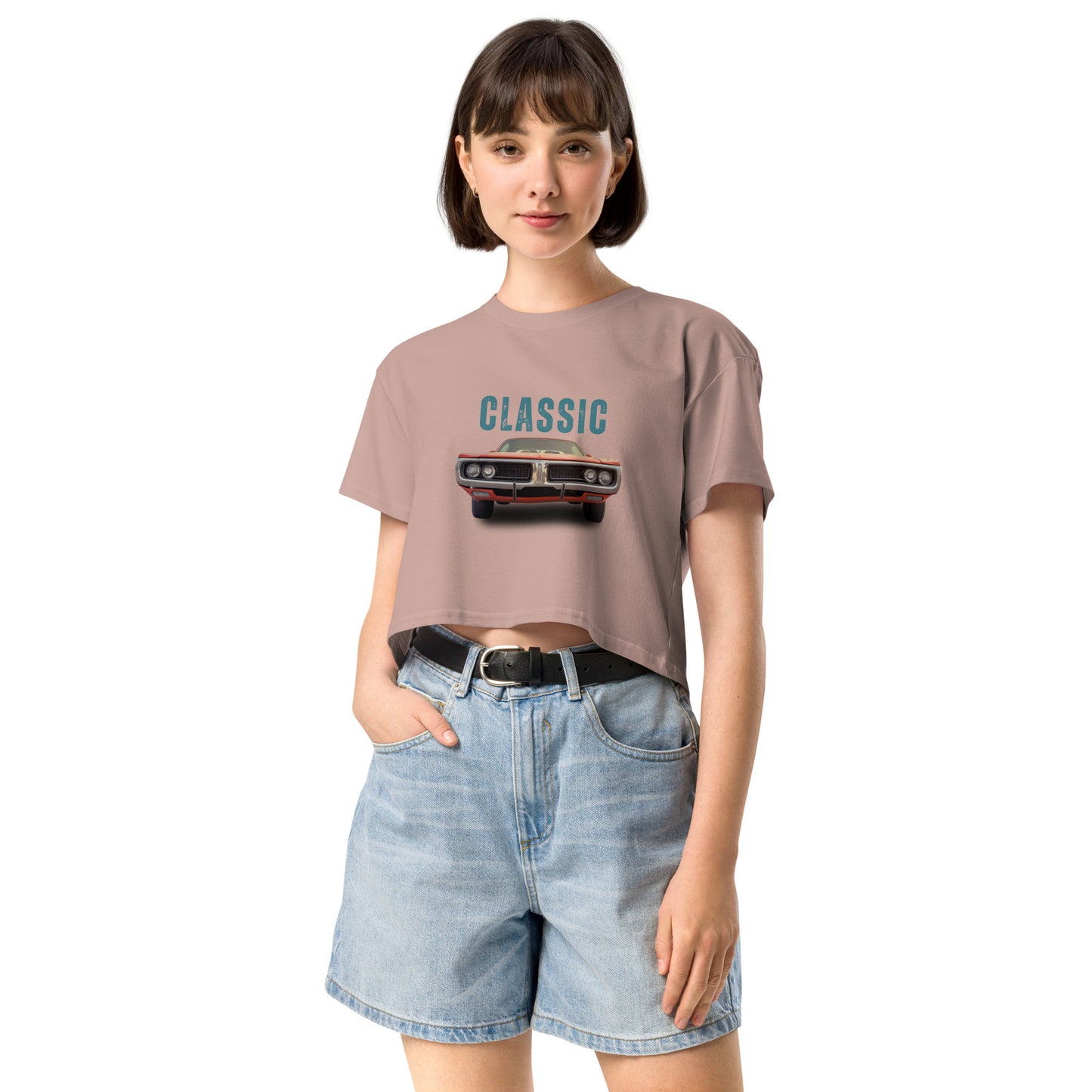 Young woman sporting a hazy pink crop top with a classic car graphic design and 'CLASSIC' text, paired with blue denim shorts for a relaxed yet fashionable look.