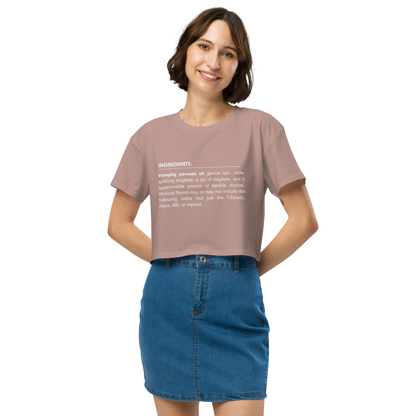 Cheerful woman in a hazy pink crop top featuring a quirky 'Ingredients' list, paired with a denim skirt for a look that combines fun and trendy style.