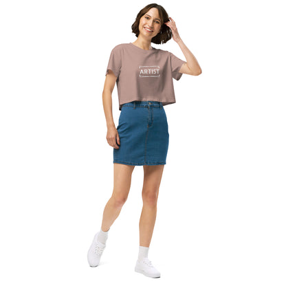 Stylish woman in a hazy pink crop top emblazoned with 'ARTIST' in bold font, paired with a denim skirt, projecting a creative and expressive vibe.