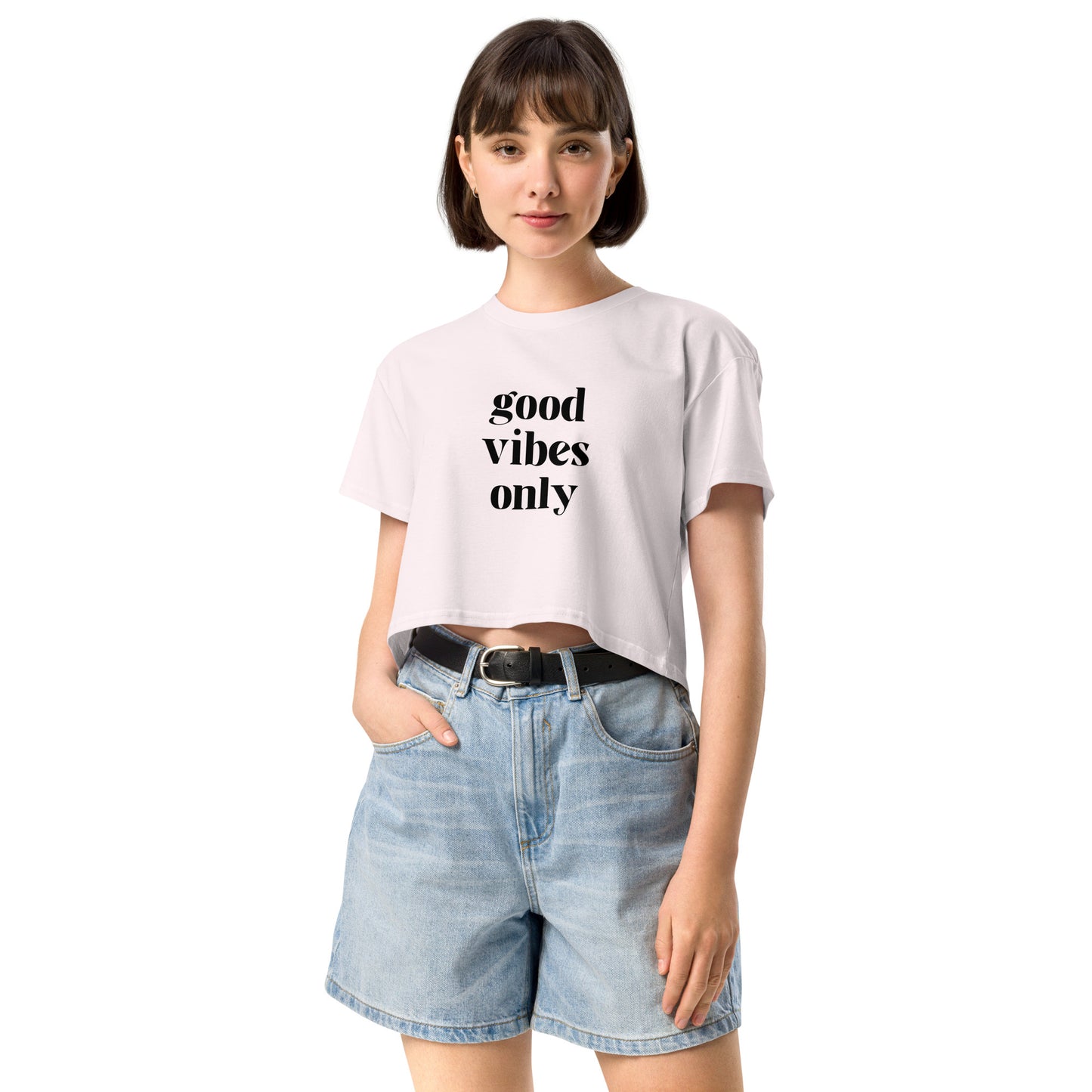 Content woman in a orchid crop top with 'good vibes only' text, coupled with light blue denim shorts, conveying a laid-back style.