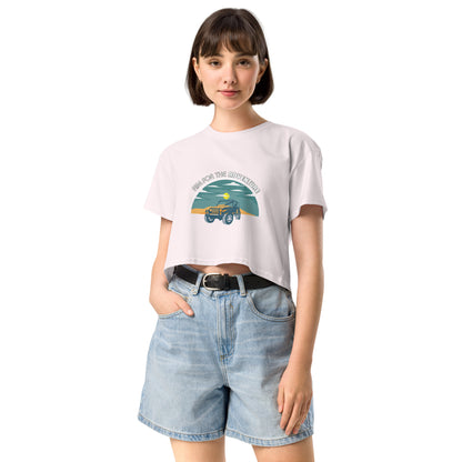 Content young woman wearing a orchid crop top with a vintage car and 'AIM FOR THE ADVENTURE' graphic, paired with light denim shorts for a laid-back, adventurous vibe.