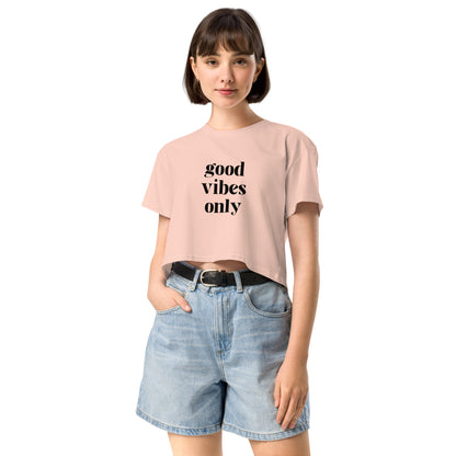 Content woman in a pale pink crop top with 'good vibes only' text, coupled with light blue denim shorts, conveying a laid-back style.