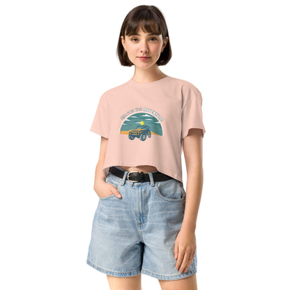 Content young woman wearing a pale pink crop top with a vintage car and 'AIM FOR THE ADVENTURE' graphic, paired with light denim shorts for a laid-back, adventurous vibe.