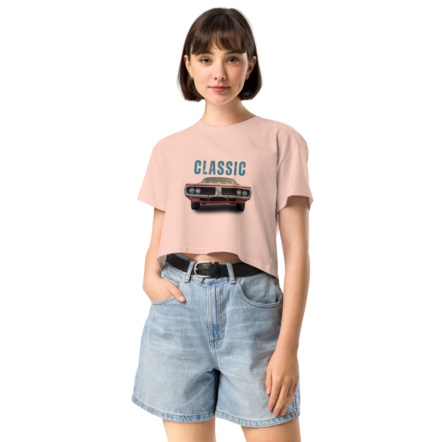 Young woman sporting a hazy pink crop top with a classic car graphic design and 'CLASSIC' text, paired with blue denim shorts for a relaxed yet fashionable look.