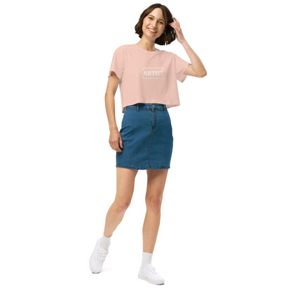 Stylish woman in a pale pink crop top emblazoned with 'ARTIST' in bold font, paired with a denim skirt, projecting a creative and expressive vibe.