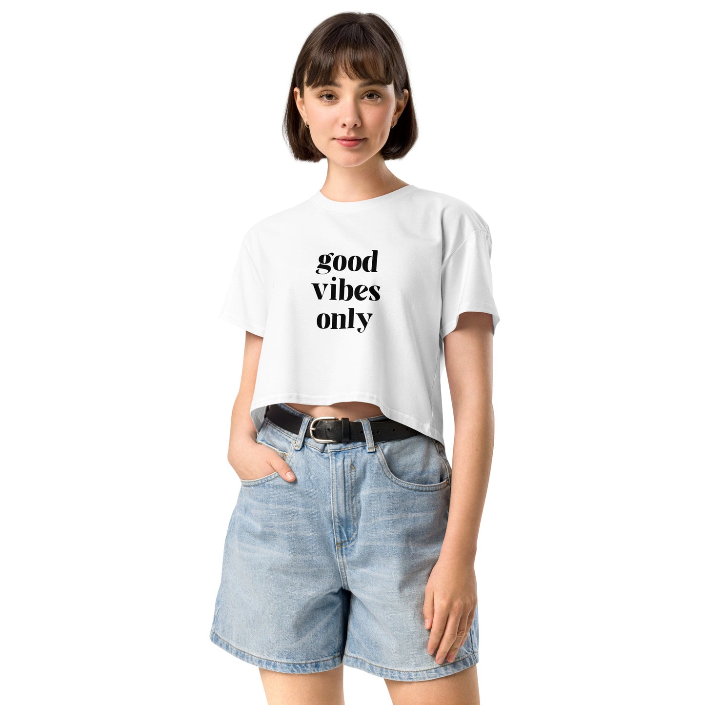 Content woman in a white crop top with 'good vibes only' text, coupled with light blue denim shorts, conveying a laid-back style.