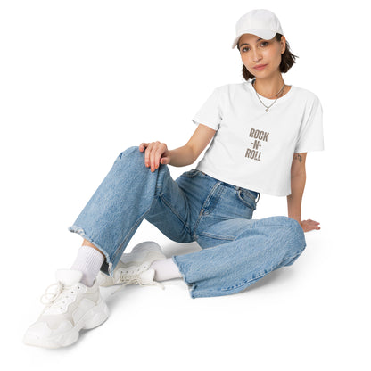 Stylish woman in a white crop top with 'Rock N' Roll' slogan, white cap, and relaxed blue jeans.