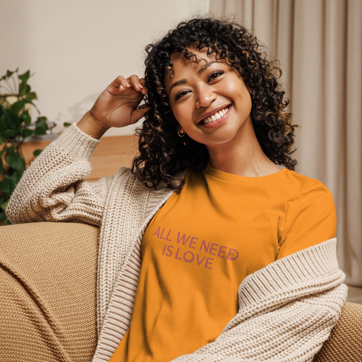 Woman smiling in heather orange relaxed t-shirt with 'All We Need Is Love' phrase