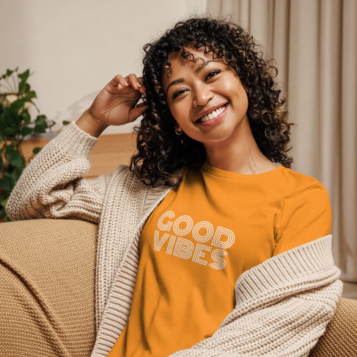 Woman smiling in a heather orange relaxed t-shirt with "Good Vibes" in white lettering, promoting a positive and cheerful style.