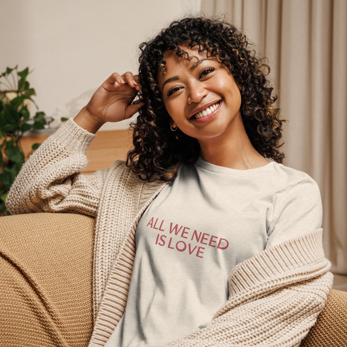 Woman smiling in heather natural relaxed t-shirt with 'All We Need Is Love' phrase