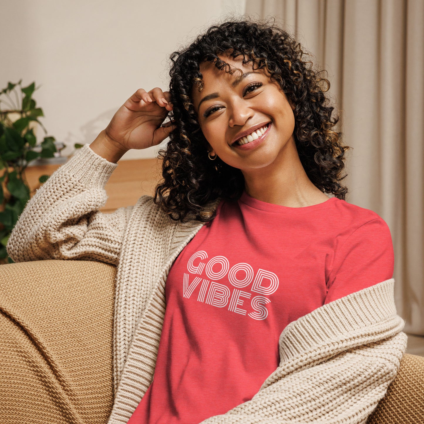 Woman smiling in a heather red relaxed t-shirt with "Good Vibes" in white lettering, promoting a positive and cheerful style.