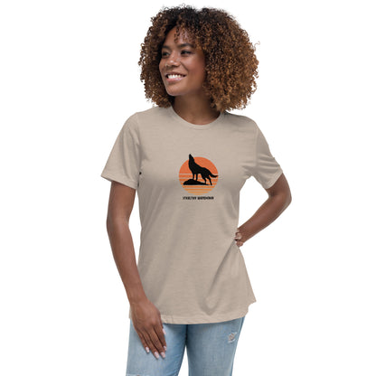 Woman wearing a stone bravery-themed relaxed t-shirt with a wolf graphic and 'Stealthy Wanderer' text in a sunset backdrop