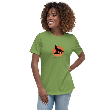 Woman wearing a leaf green bravery-themed relaxed t-shirt with a wolf graphic and 'Stealthy Wanderer' text in a sunset backdrop